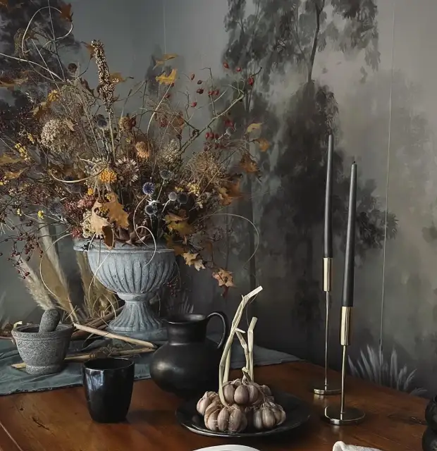 Fotografía de mesa rústica con centro floral seco, velas negras y objetos decorativos en tonos tierra para interiorismo natural y elegante.