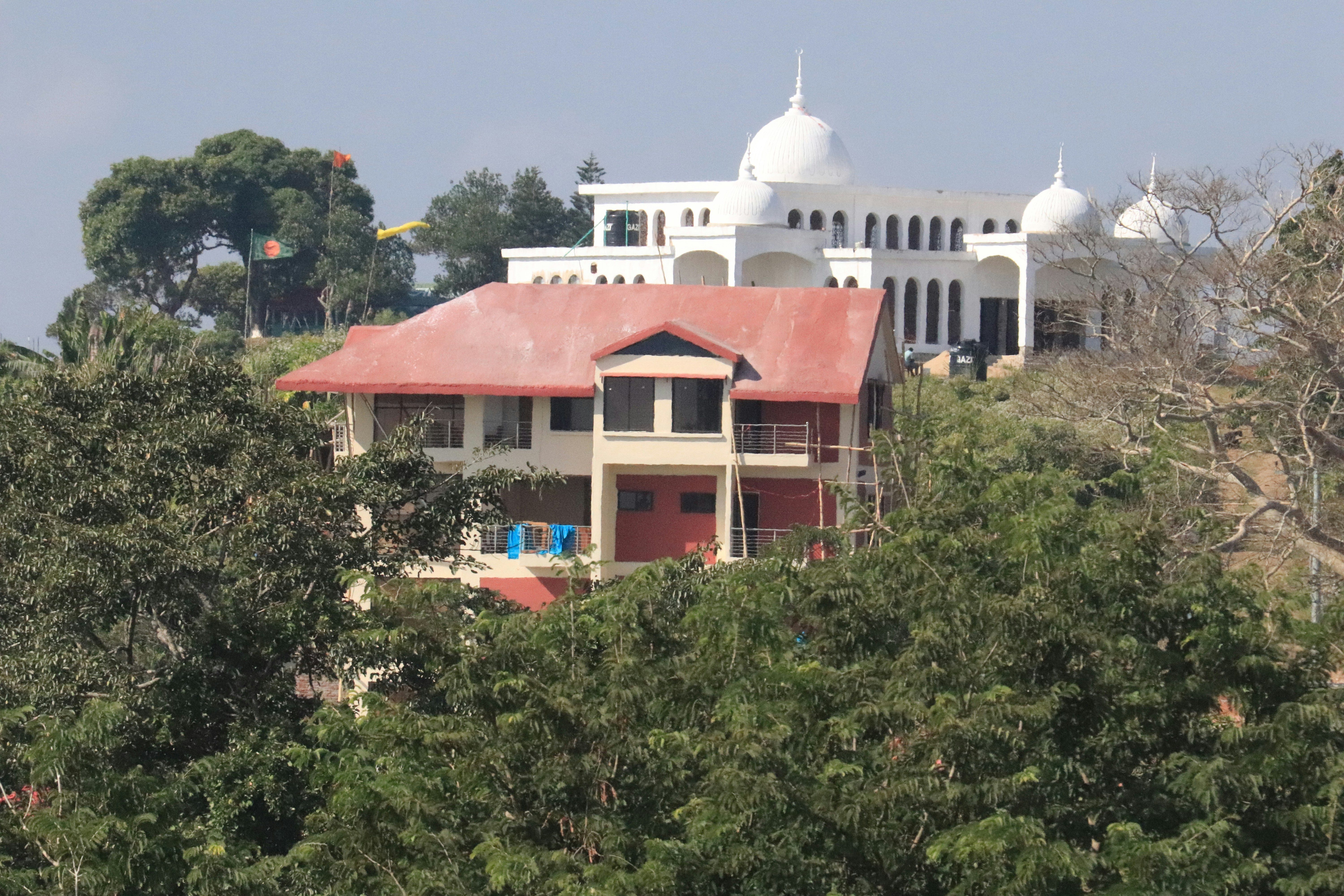 a duplex/triplex white building with a red roof surrounded by trees
