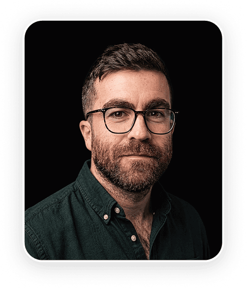 Two people are laughing and enjoying a moment together, holding a phone, in a dimly lit setting.