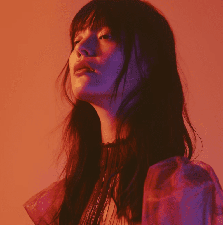 A person with long, dark hair is bathed in soft, warm red lighting, creating a dramatic and moody atmosphere.