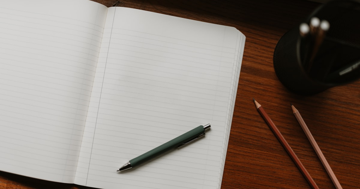 Open notebook with pen on a wooden desk, blending analog planning with digital budgeting.