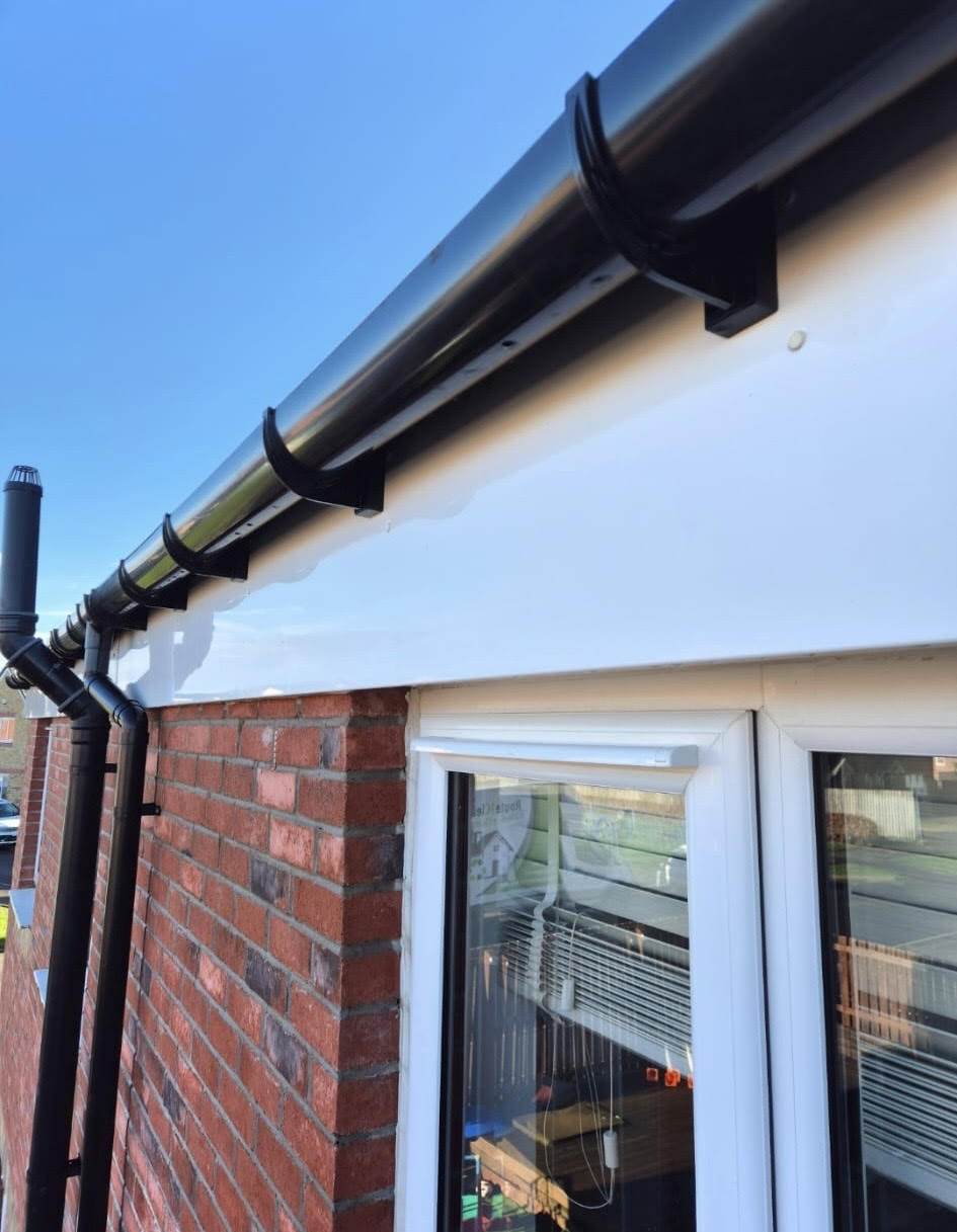 Close-up of a house corner showing black guttering on a red brick wall under a clear blue sky.