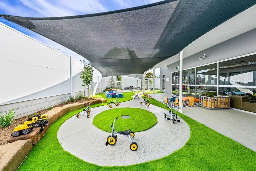 Outdoor play area with tricycles, shade sails and activity zones at Kaleidoscope Kids childcare centre in Brisbane.