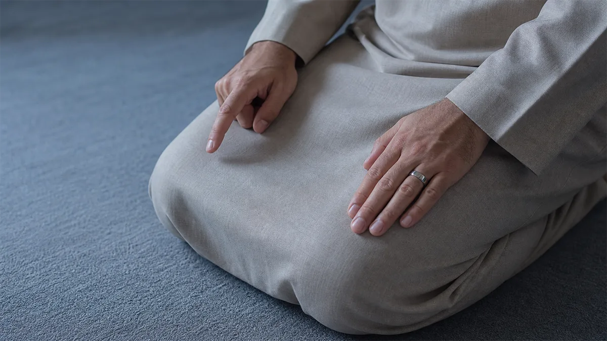 Hands in the tashahhud position, with one index finger extended and a plain steel ring untouched