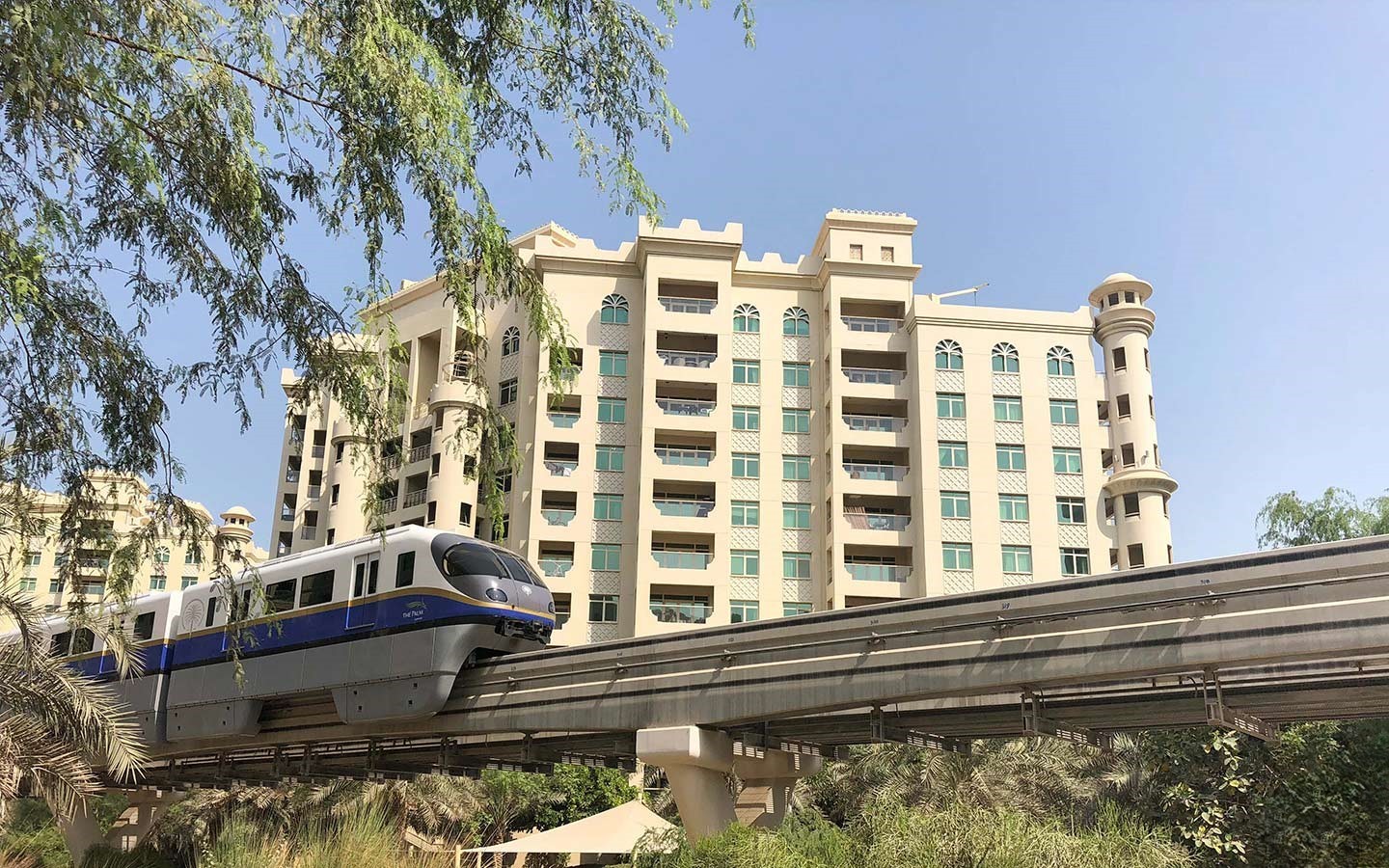 The elevated Palm Jumeirah Monorail passes in front of a large, distinctive hotel building, showcasing the island's transportation.