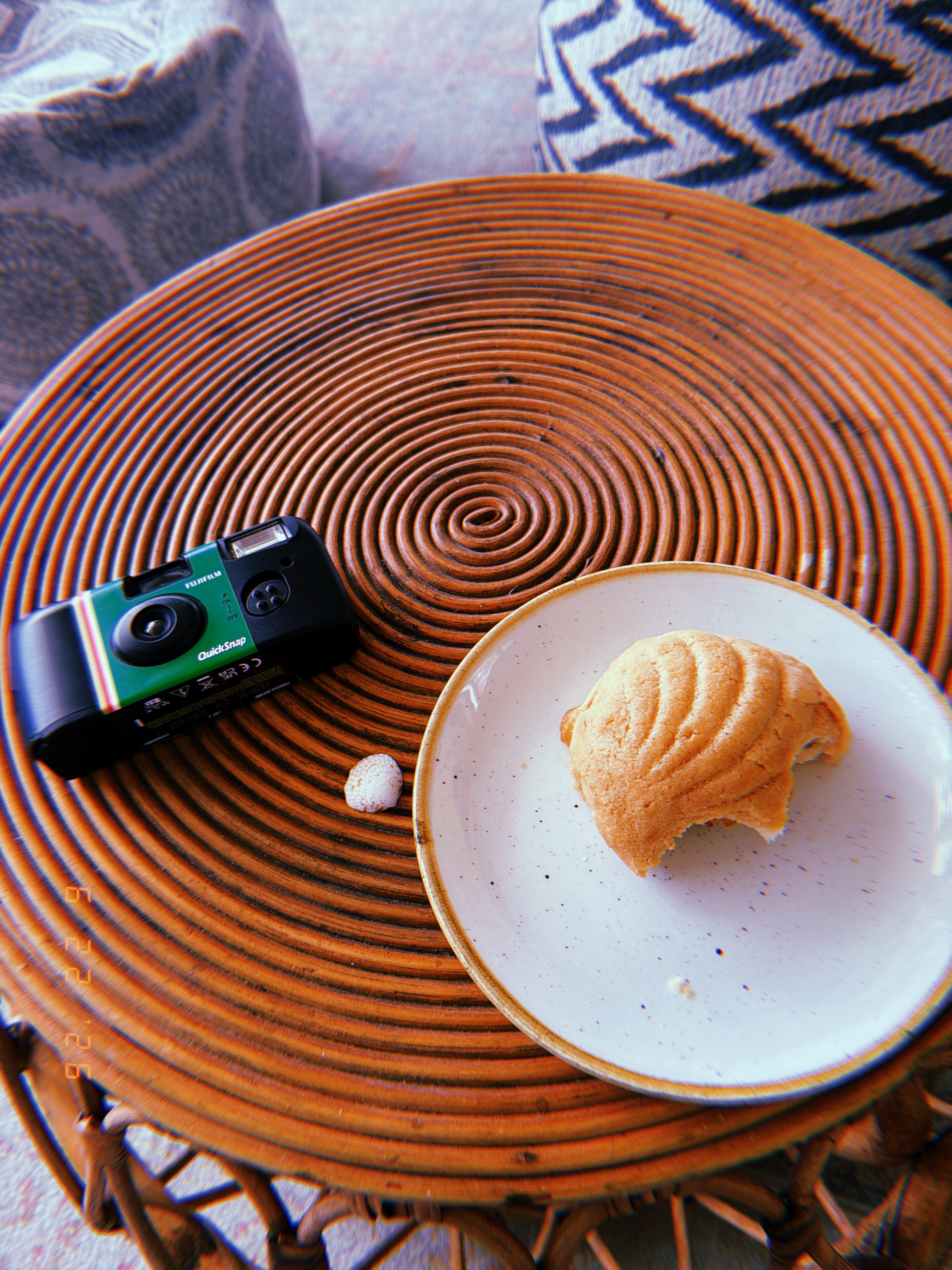 A spiral rattan table with a disposable camera and shell-shaped bread on a plate