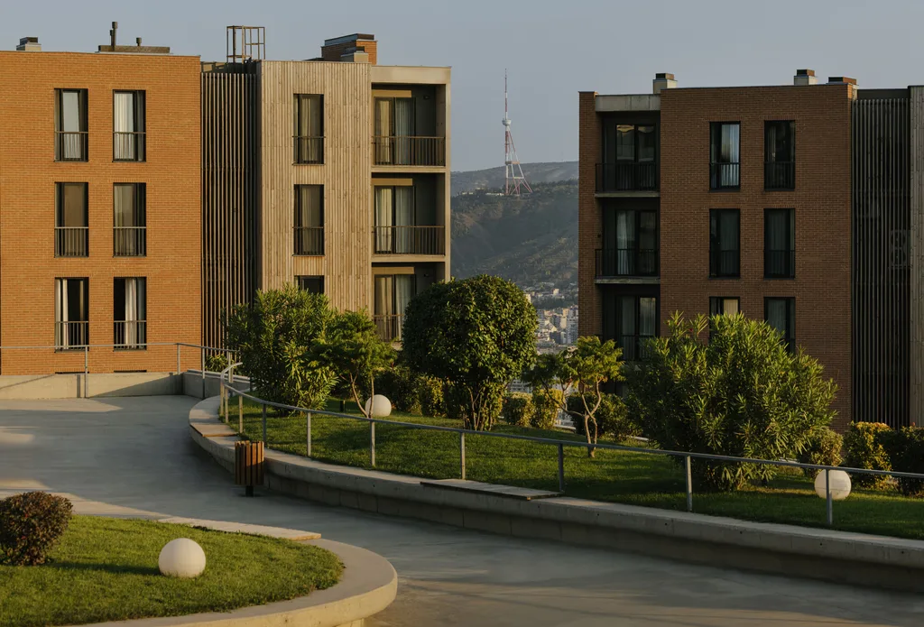 A modern building with greenery, pathways, and mountains in the background under a clear blue sky.