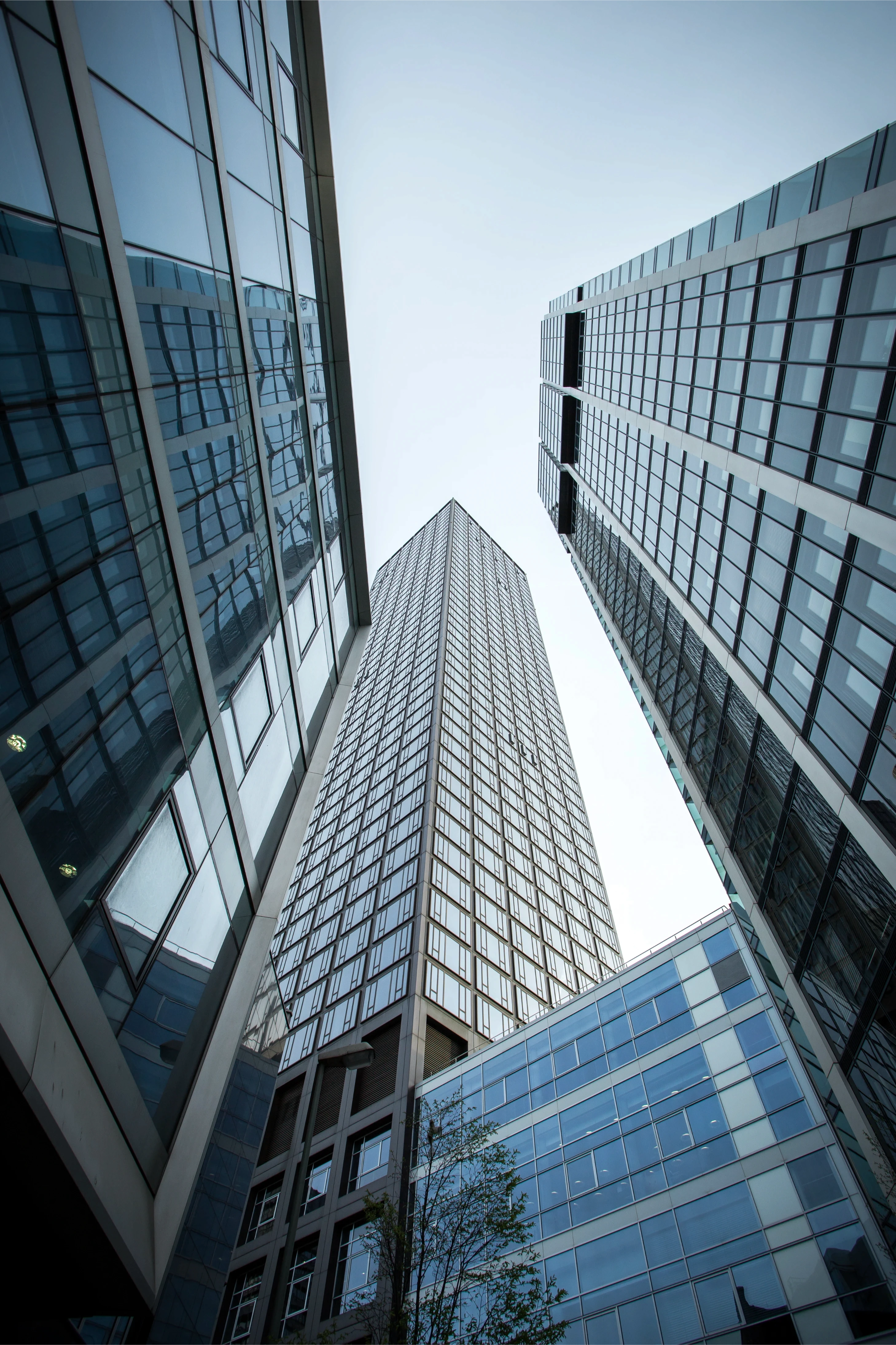 Looking up at three modern skyscrapers with glass facades, converging towards the sky. The image conveys a sense of grandeur and urban architecture.