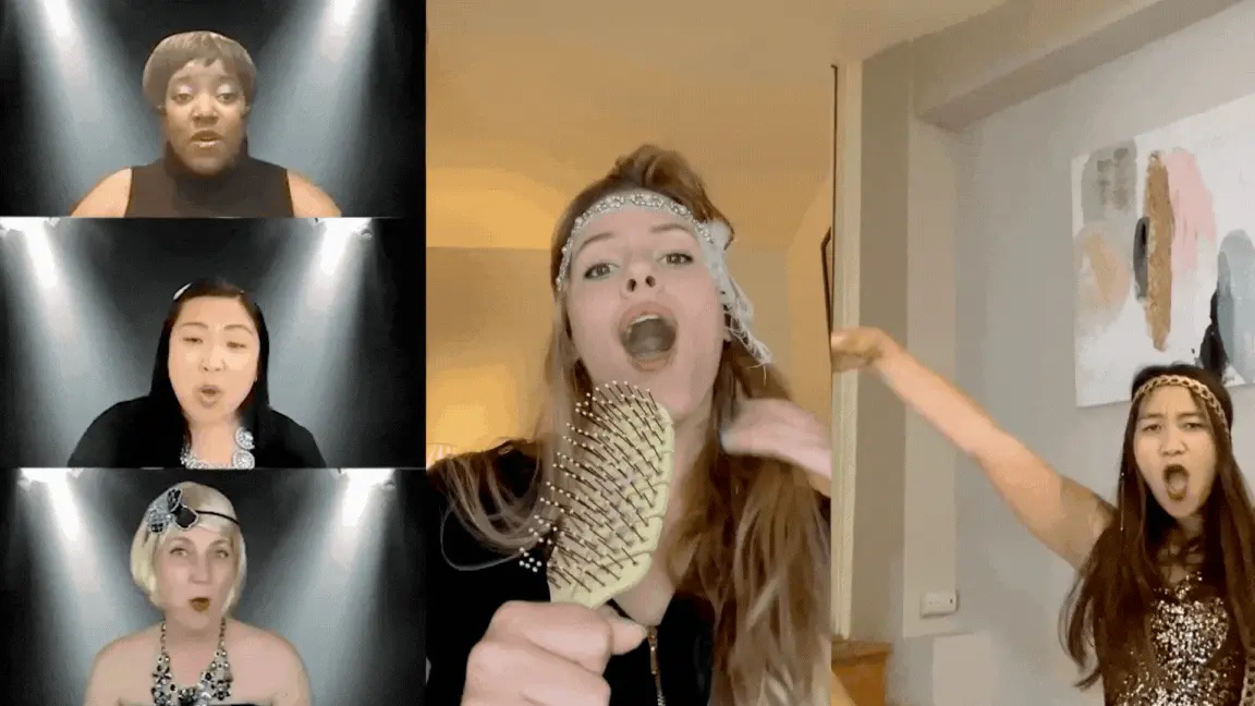 A dynamic virtual choir performance with six women singing from separate video frames. On the left, four singers are shown in individual black-background boxes. On the right, two women perform with playful flair—one singing into a hairbrush while wearing a beaded headband, the other dancing with dramatic expression in a sparkly outfit. The overall theme is joyful and theatrical.