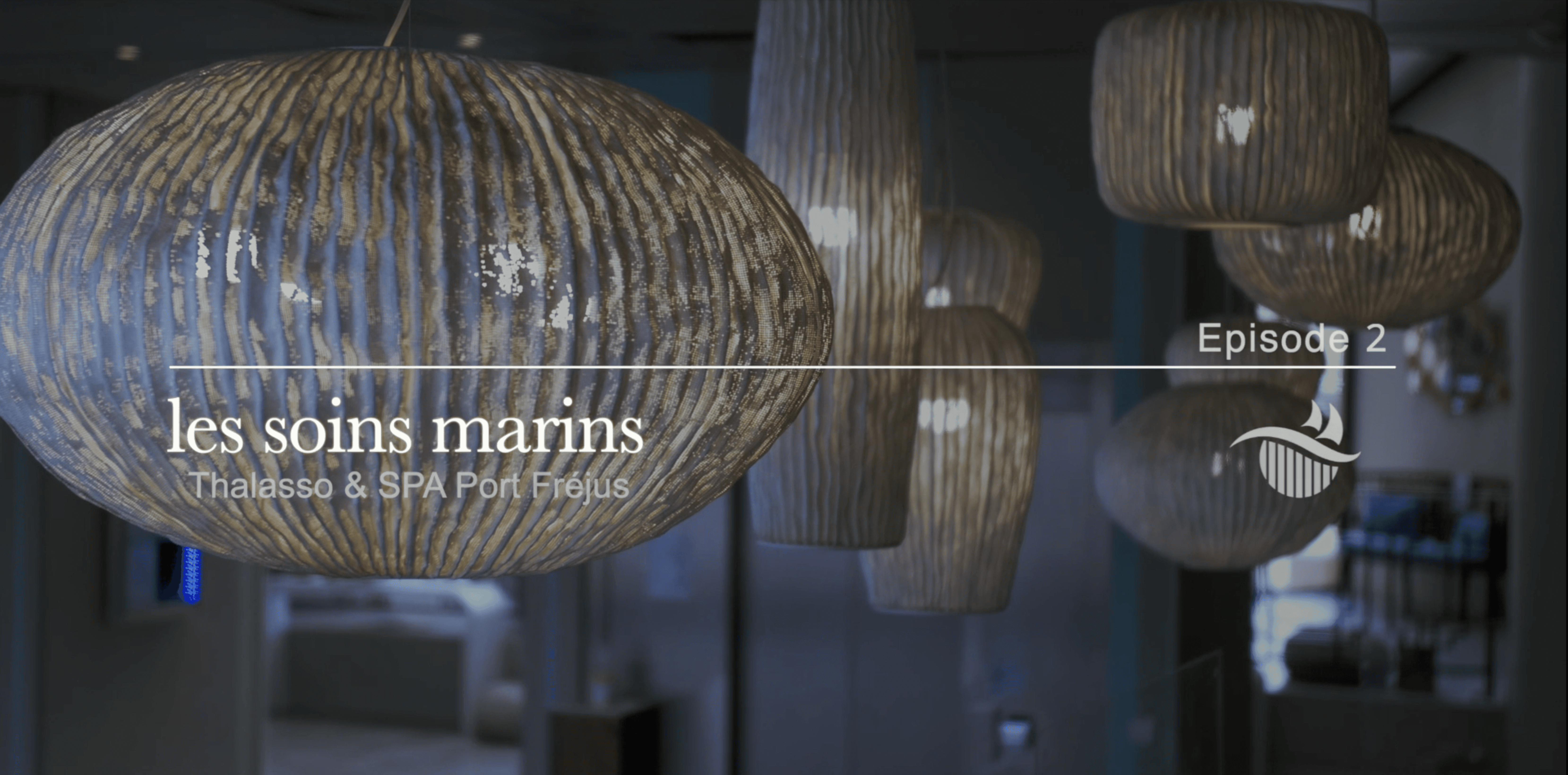 Hanging lamps with a textured, wooden finish illuminate a modern interior space bearing the text "les soins marins, Thalasso & SPA Port Fréjus, Episode 2" on the left side.