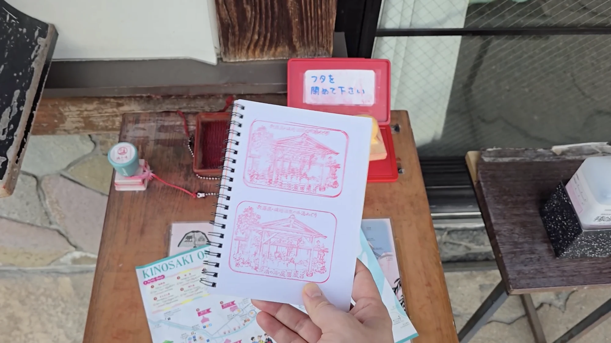 An open stamp book showing red bathhouse stamps collected on the Kinosaki sotoyu circuit.