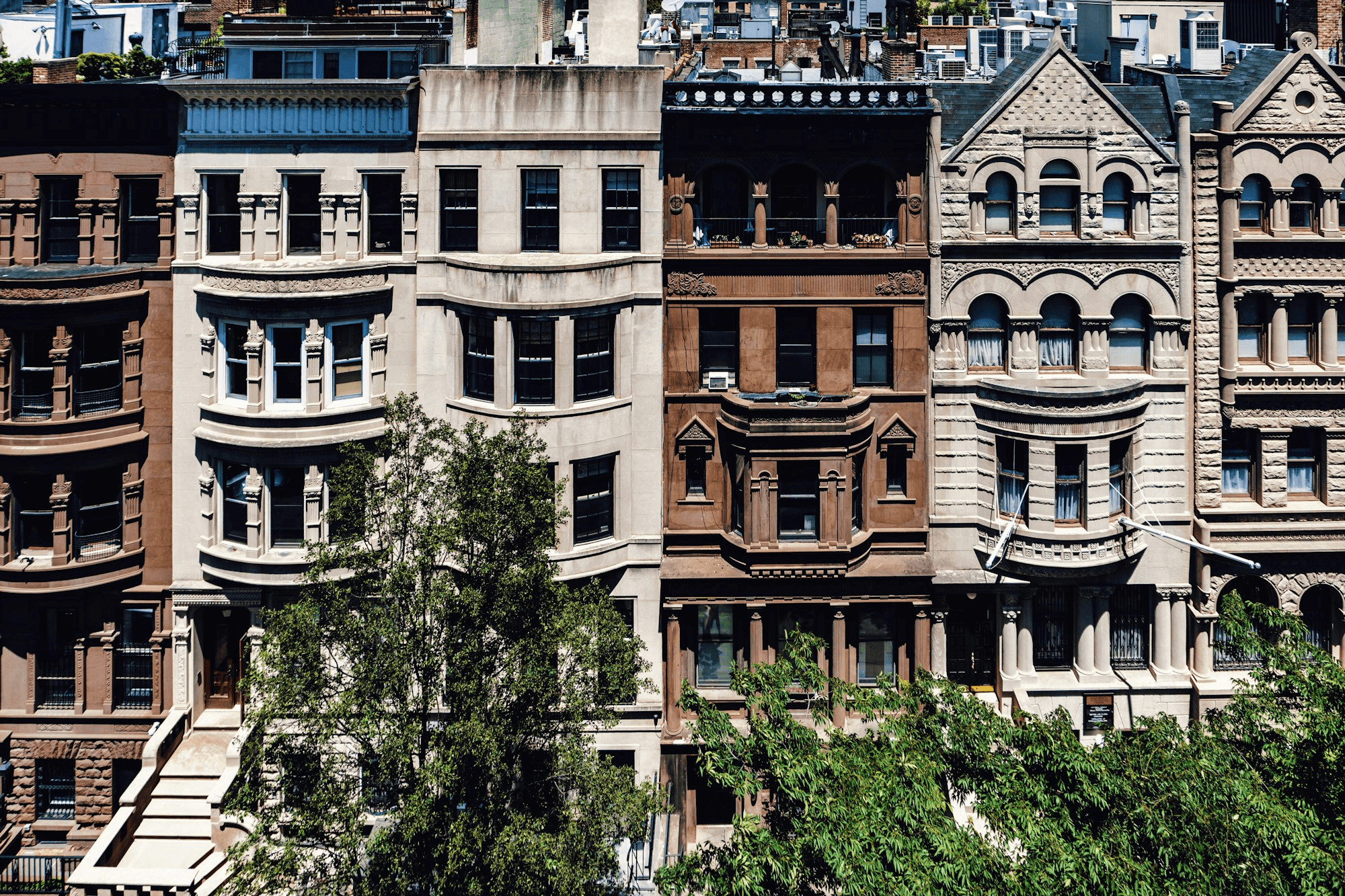 Historic New York residential facades with bay windows and leafy street trees.