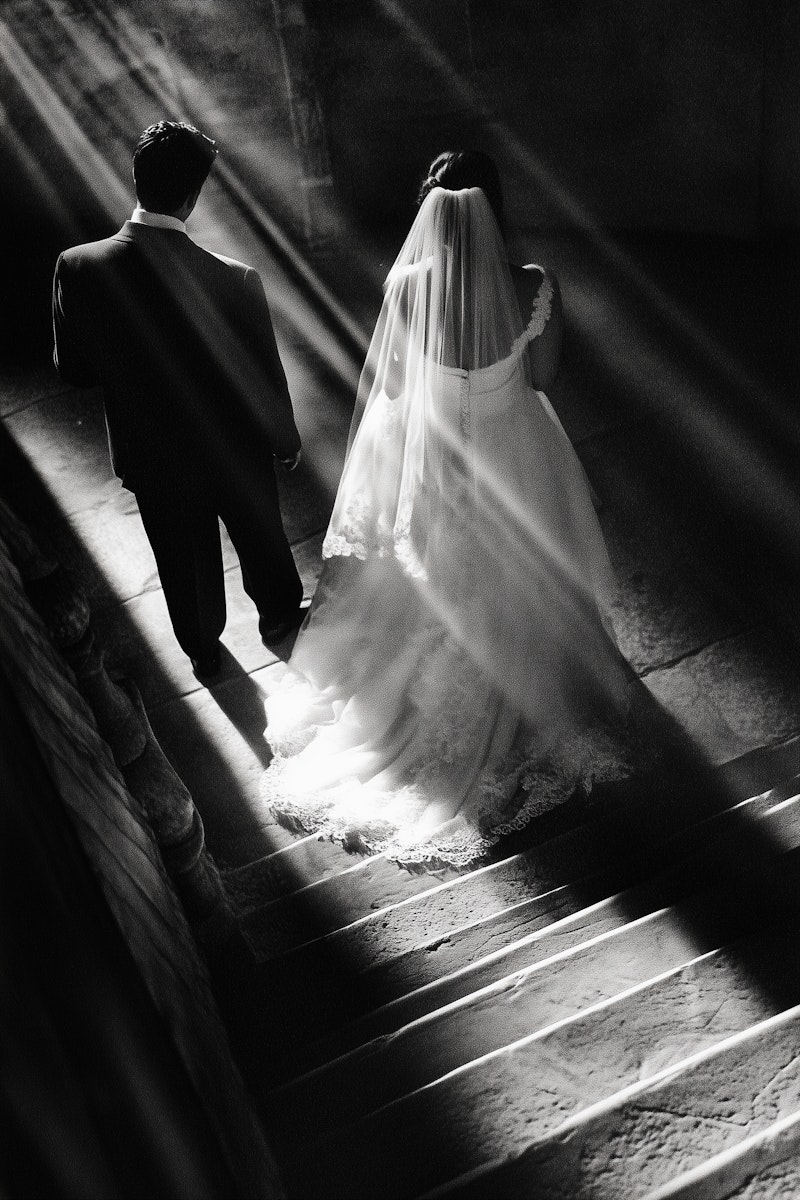 Elegant black and white photo of a bride and groom descending a staircase, with dramatic lighting and shadows.