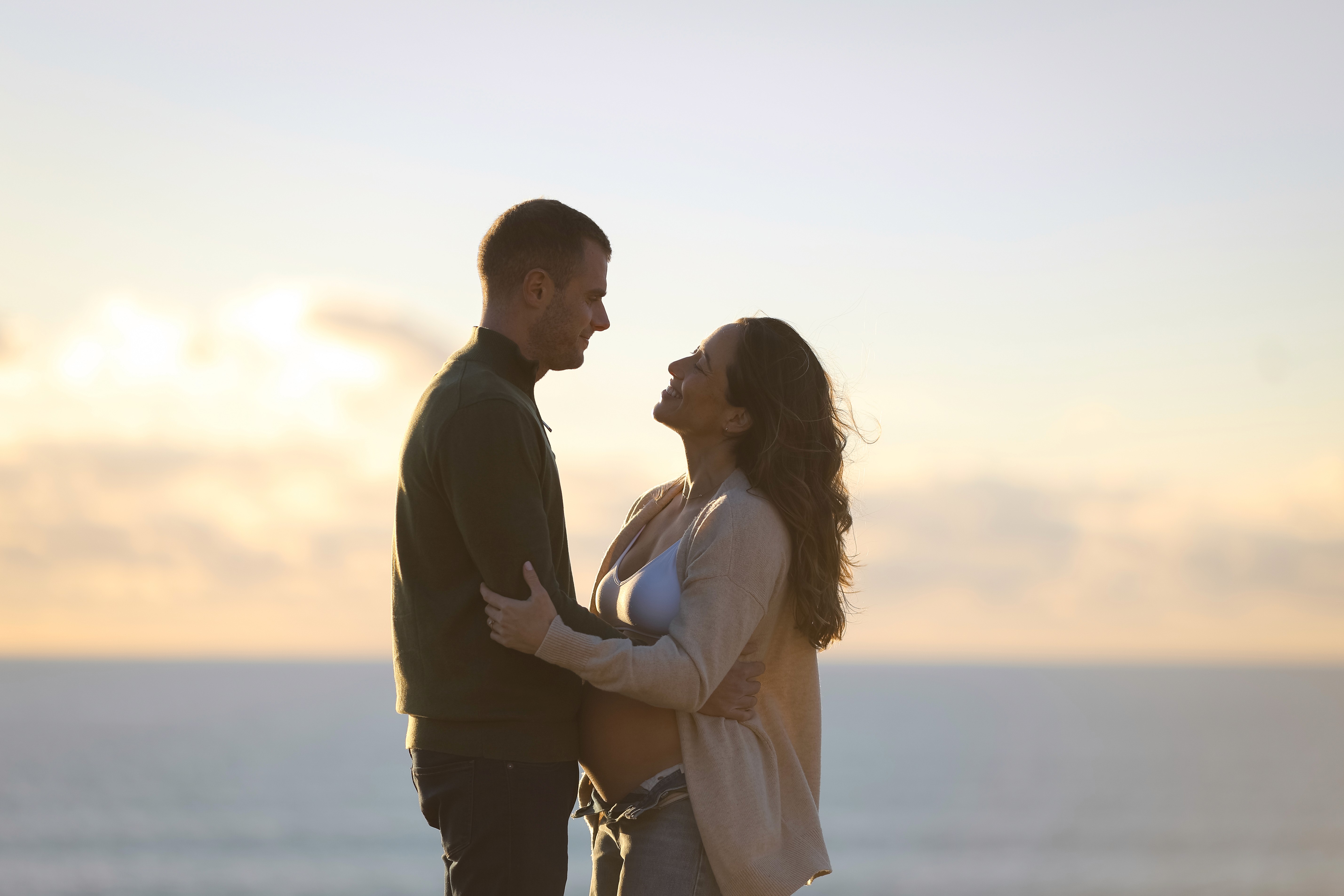 Mom lifting her toddler son during golden hour near the ocean.