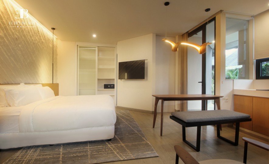 Modern kitchen and dining area featuring light wooden cabinetry, a black refrigerator, a two-burner cooktop, and a curved, illuminated pendant light fixture above the wooden dining table.