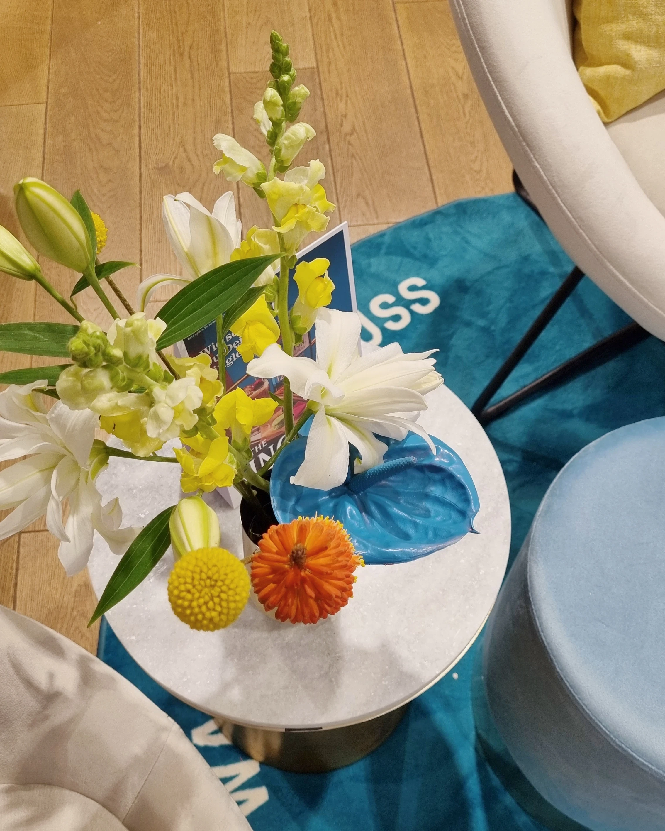 Top view of a marble side table with flowers and orange blossom on a teal Singleton rug.