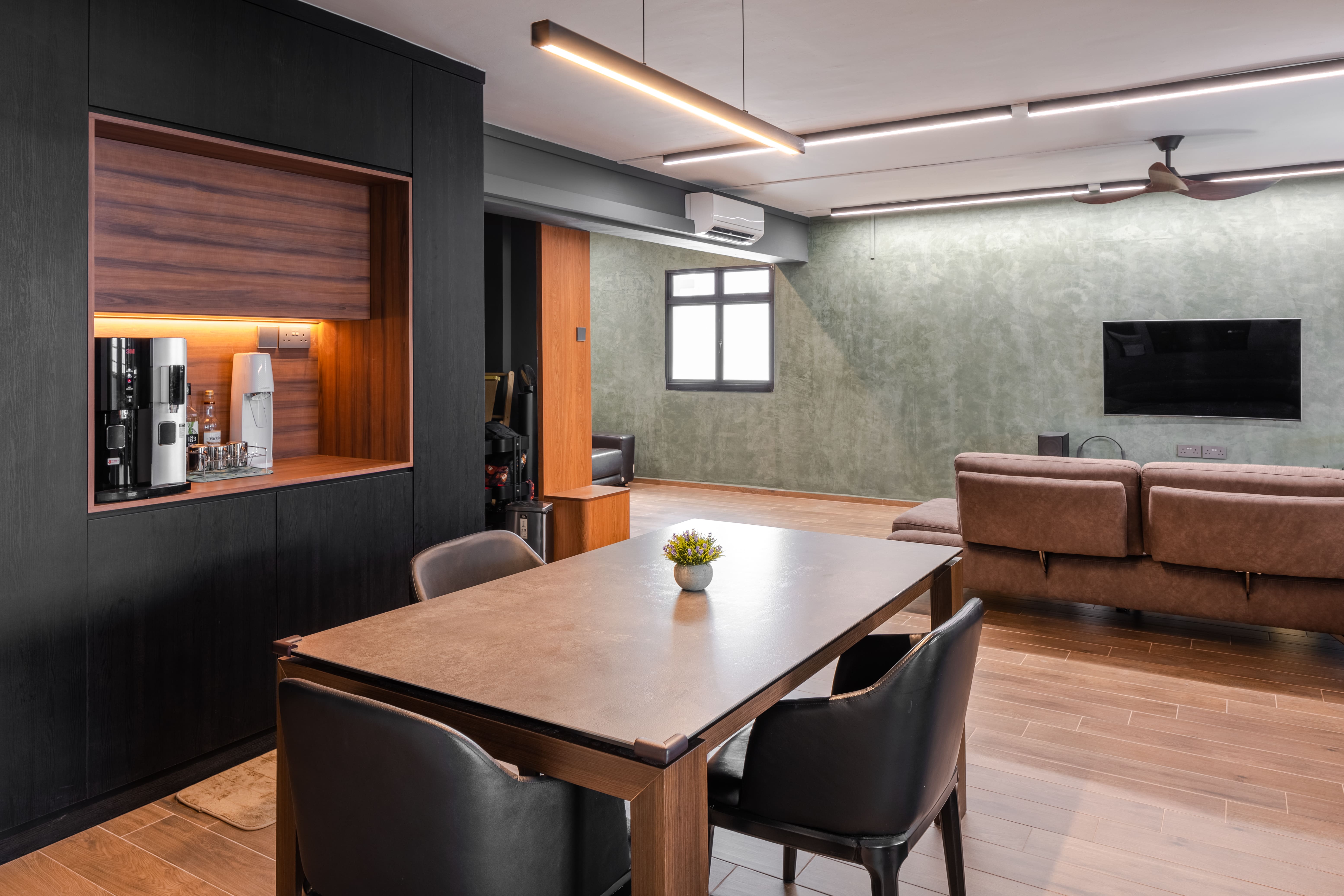 Dining area featuring dark built-in cabinetry with a coffee nook, stone-top dining table, and warm linear pendant lighting.