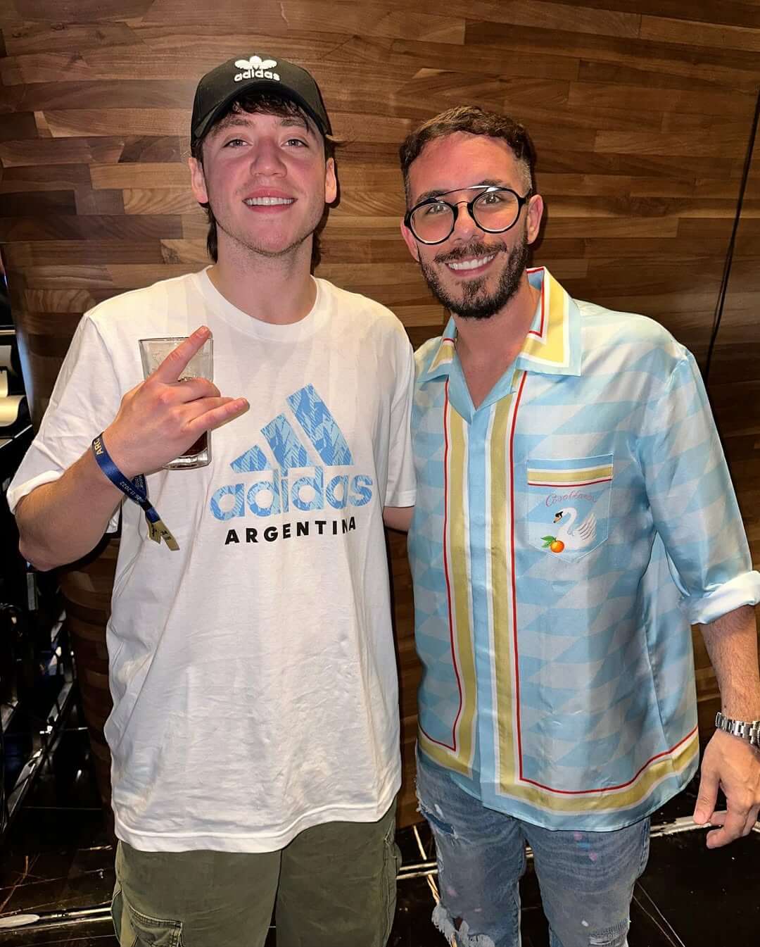 Fer Palacio con Paulo Londra en Qatar, ambos vistiendo ropa casual y haciendo señas de festejo.