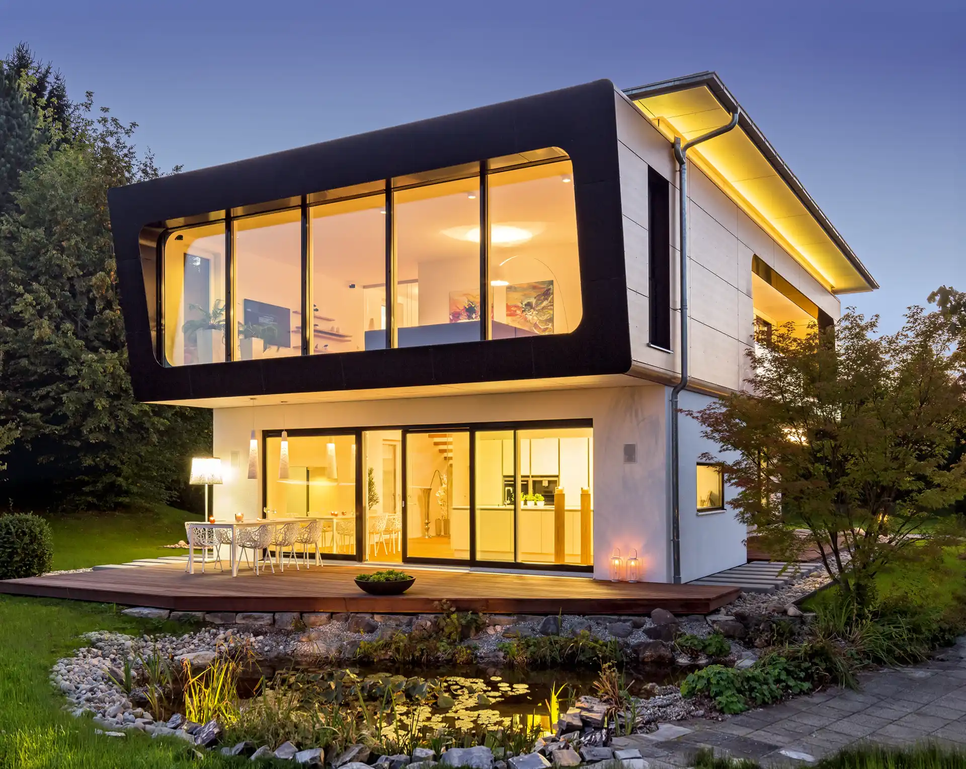 Modernes Haus mit Überhang und großem Fenster im Obergeschoss, daneben eine Terrasse mit Gartenteich.