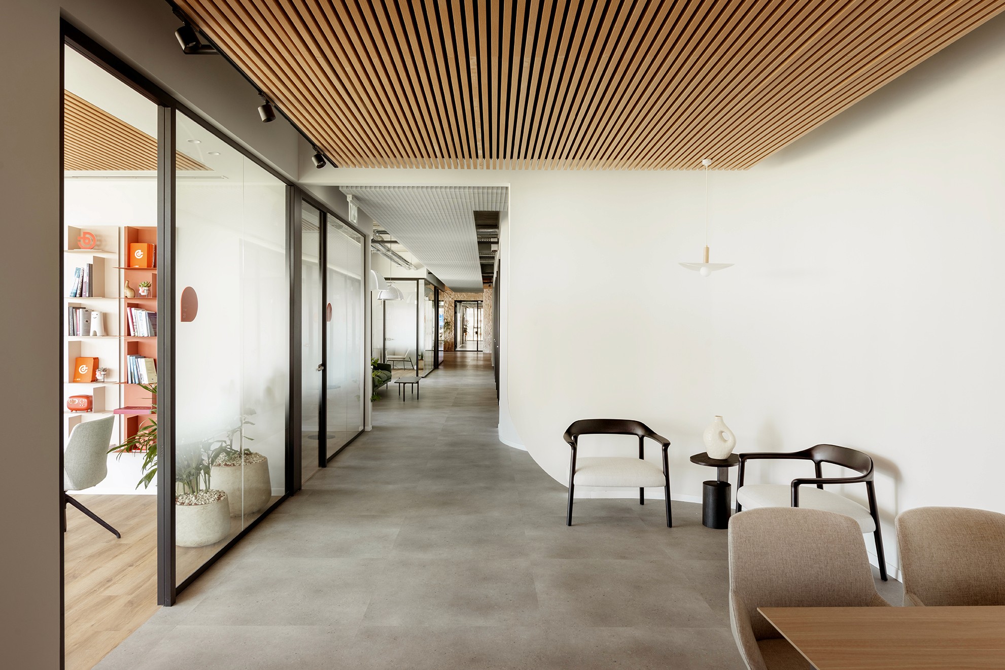 עיצוב מעברים ומבואות: שילוב תקרת רפפות עץ לינארית המסתירה מערכות, עם מחיצות זכוכית אקוסטיות למקסימום שקיפות