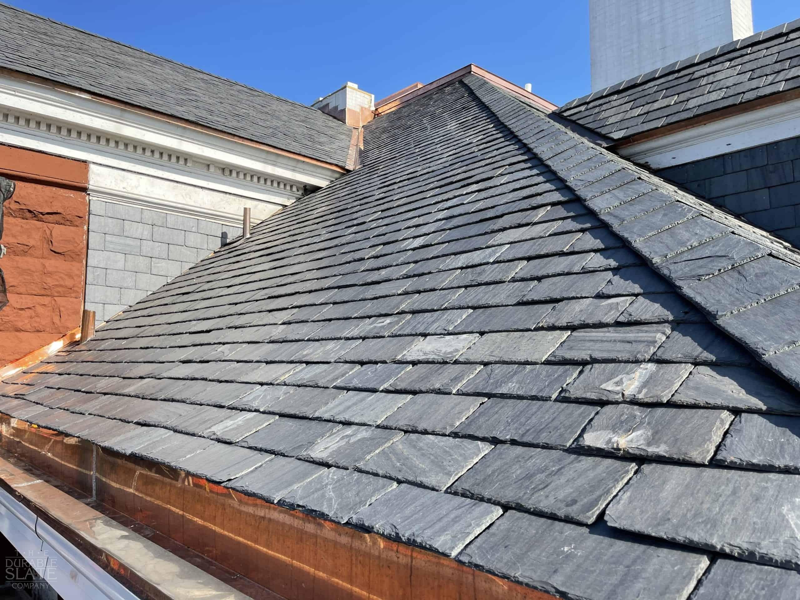 Close-up of a slate roof with a pitched design against a clear blue sky, highlighting the texture and layers.