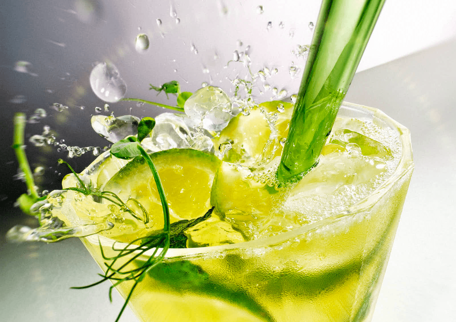 A refreshing green drink garnished with mint, ice, and a sprig of rosemary, splashing in a glass.