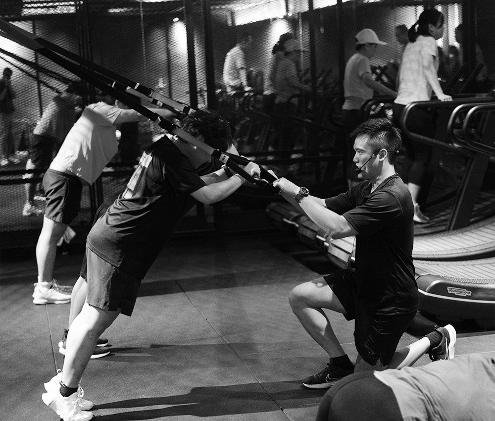A Coach Correcting The Members Grip In A TRX Workout Group Class