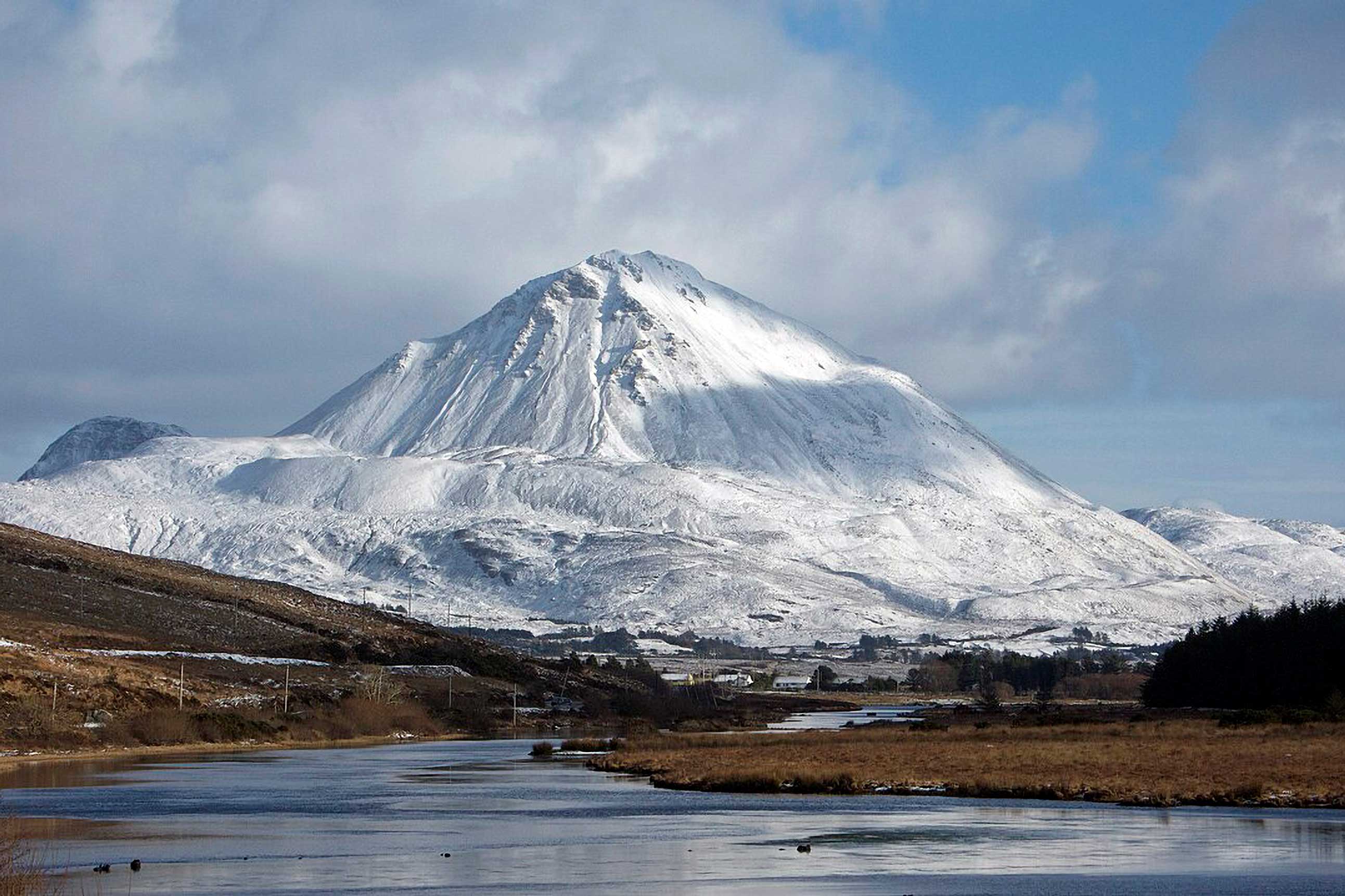 Snow-covered mountain rising above a river and open countryside.