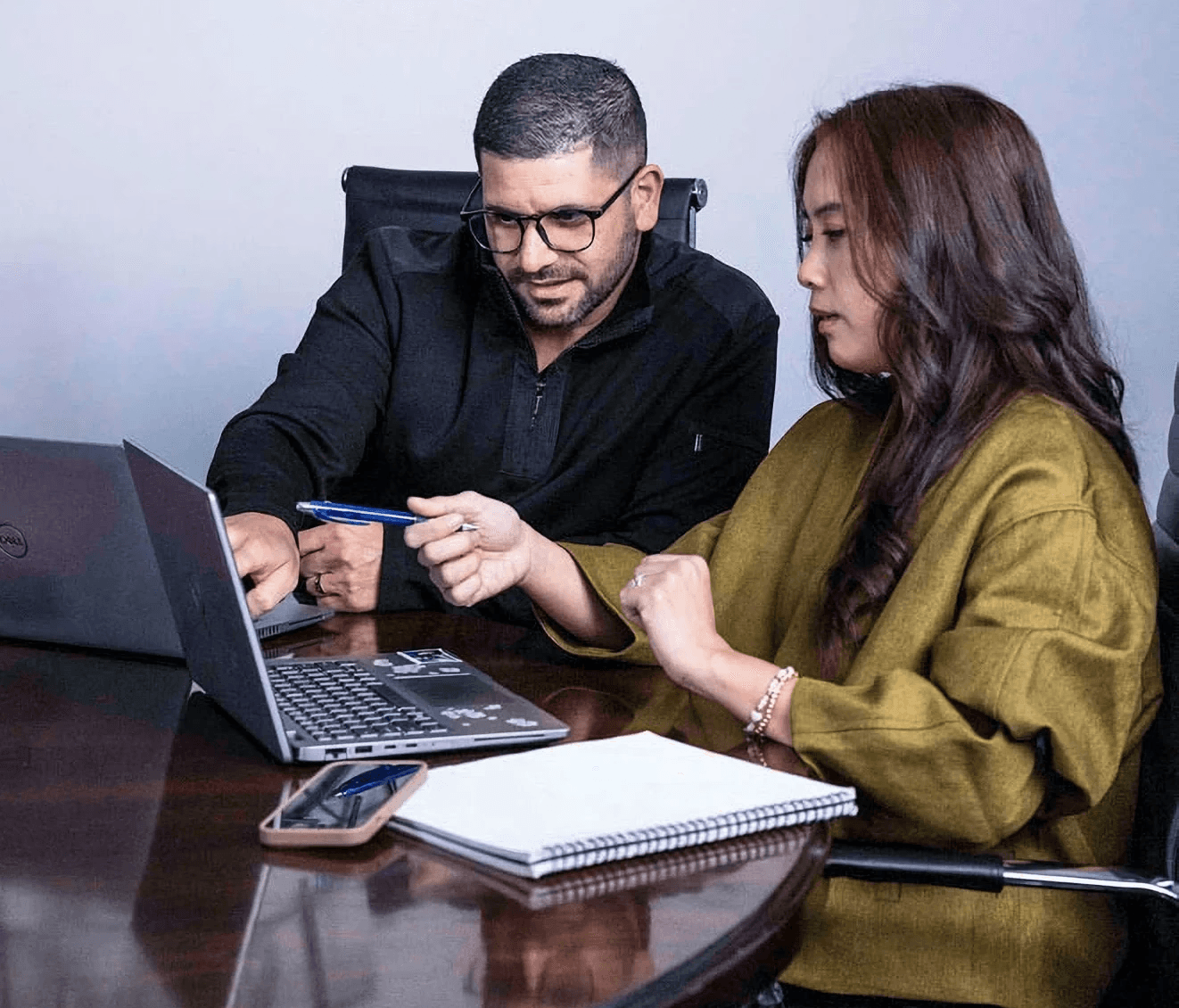 Two business professionals collaborating at an office table while reviewing data on a laptop.