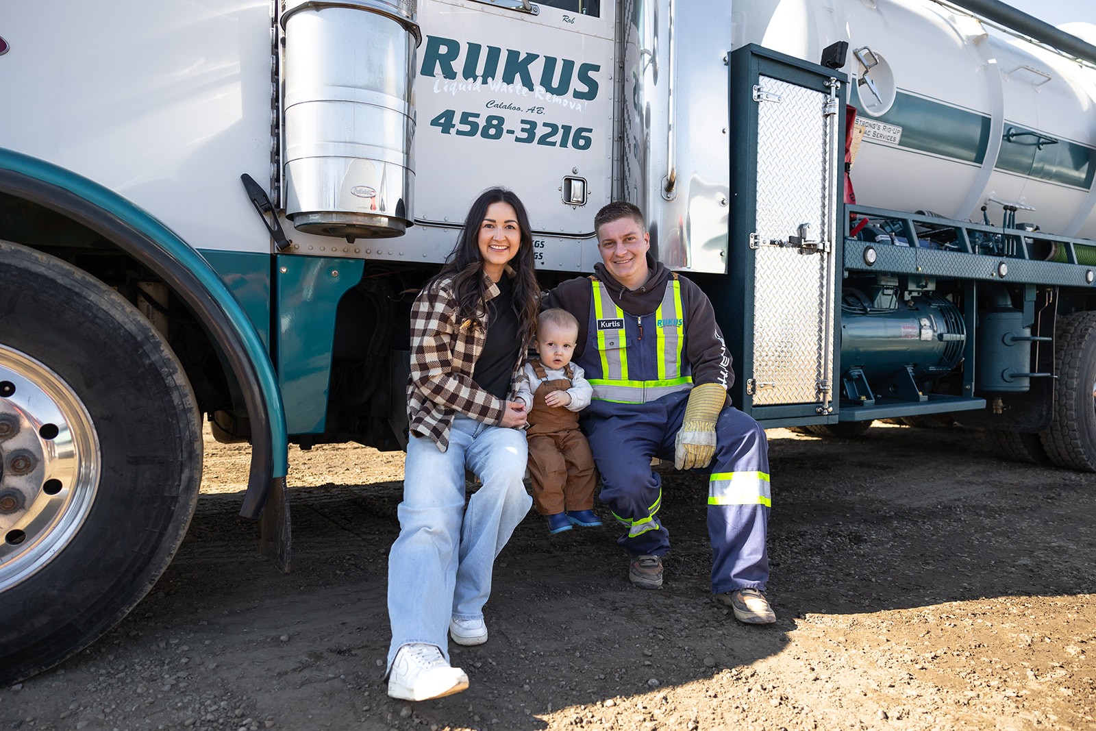 Rukus Liquid Waste Removal owners Kurtis and Bri with their young son in front of a company vacuum truck in Calahoo, Alberta, serving Edmonton and surrounding areas.