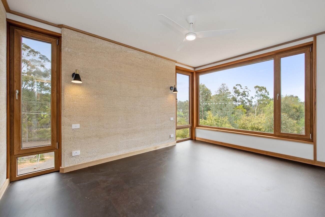 Interior living space with exposed hempcrete wall, timber-framed windows, and polished concrete floor in the Castlemaine Cast and Block House