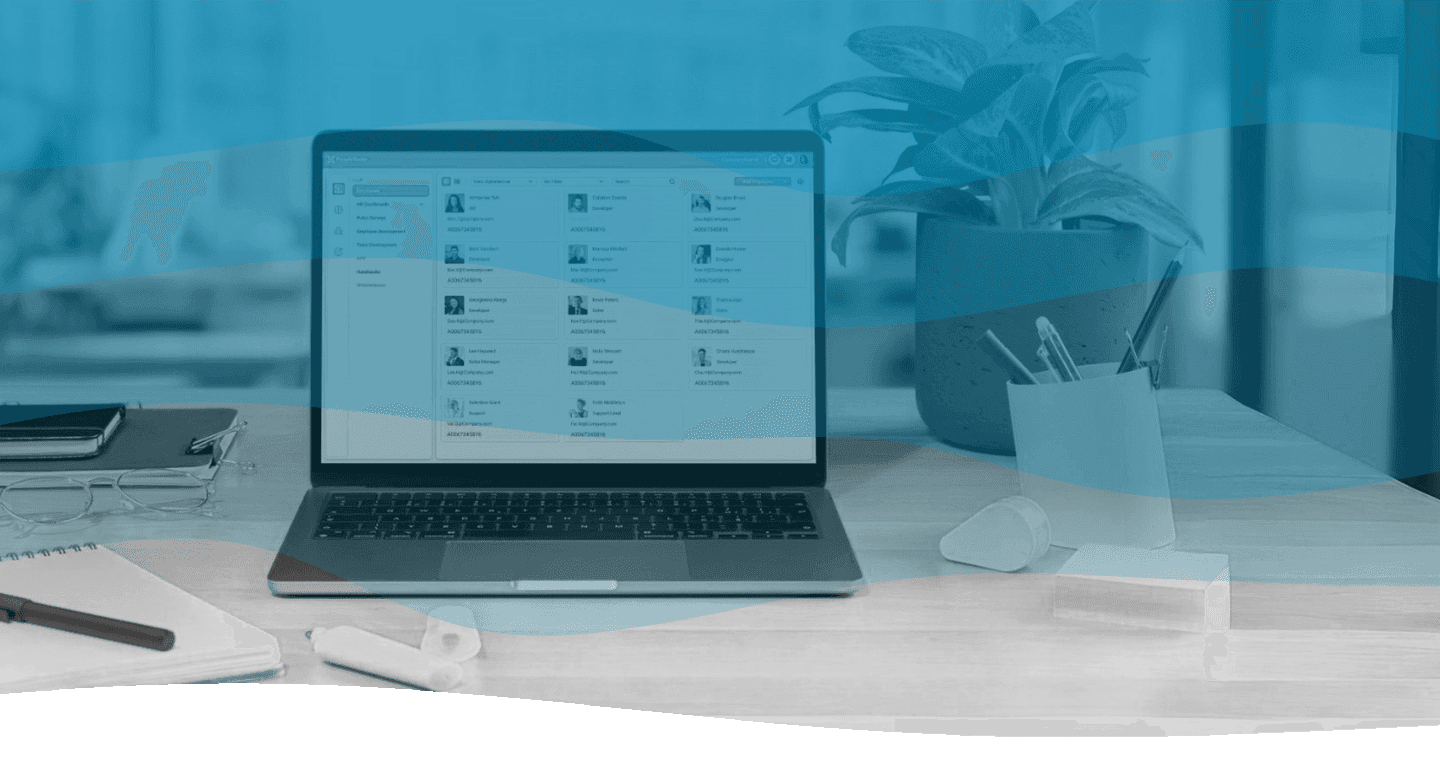 The image shows a modern office workspace with a laptop displaying a HR management application, surrounded by office supplies, a potted plant, and soft lighting, conveying productivity and organization.