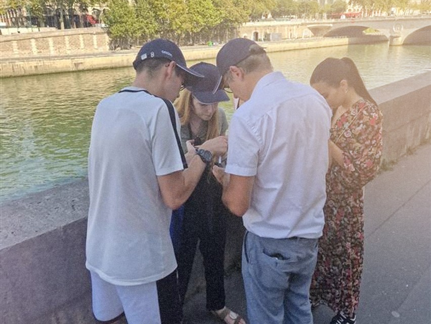 Un groupe de quatre personnes, debout près d'un fleuve, interagissant ensemble tout en utilisant leurs téléphones mobiles.
