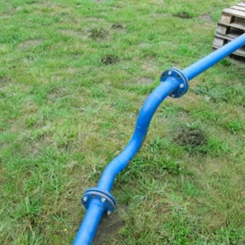 A curved blue pipe with flanges, resting on green grass. It appears to be part of a water system.
