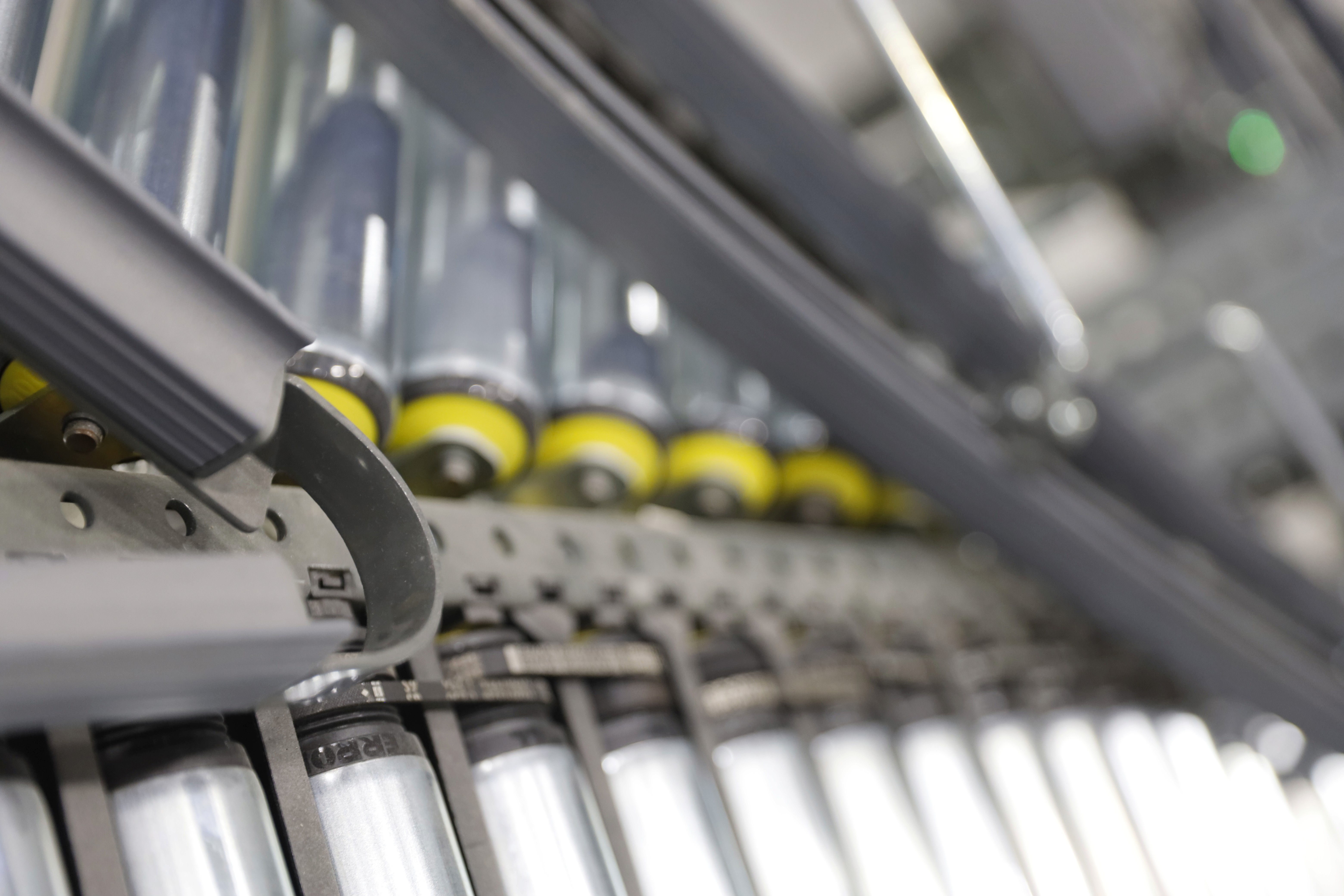 Närbild av en maskin som bearbetar material. Flera spolar syns i fokus med gula och vita detaljer.
