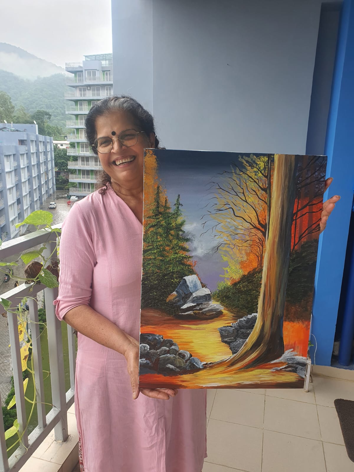 Creative Pod student holding a scenic landscape painting made with poster colors on the balcony of The Creative Pod studio.