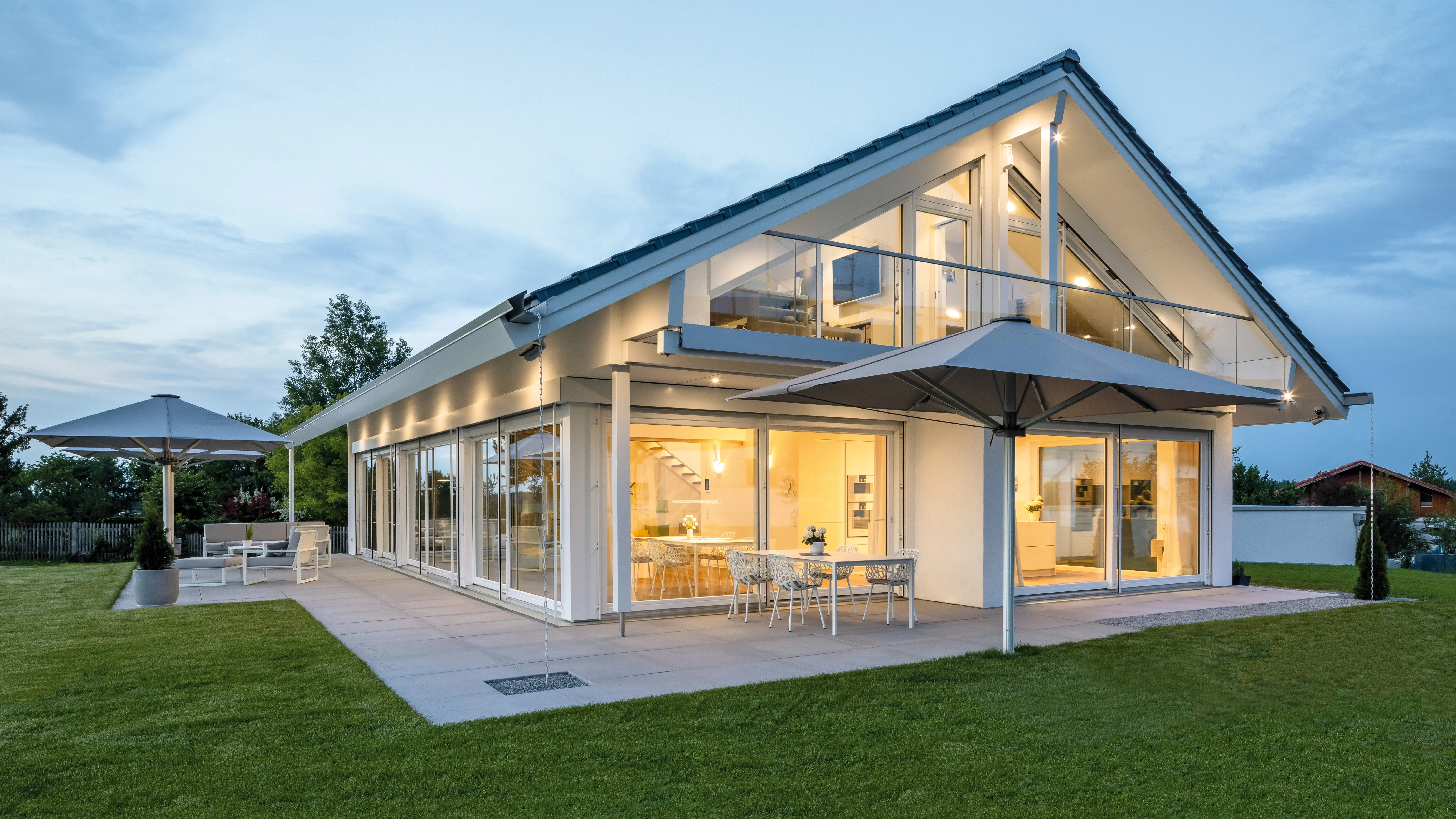 Modernes Einfamilienhaus mit großen Glasflächen und Terrasse mit Loungemöbeln und Sonnenschirmen.