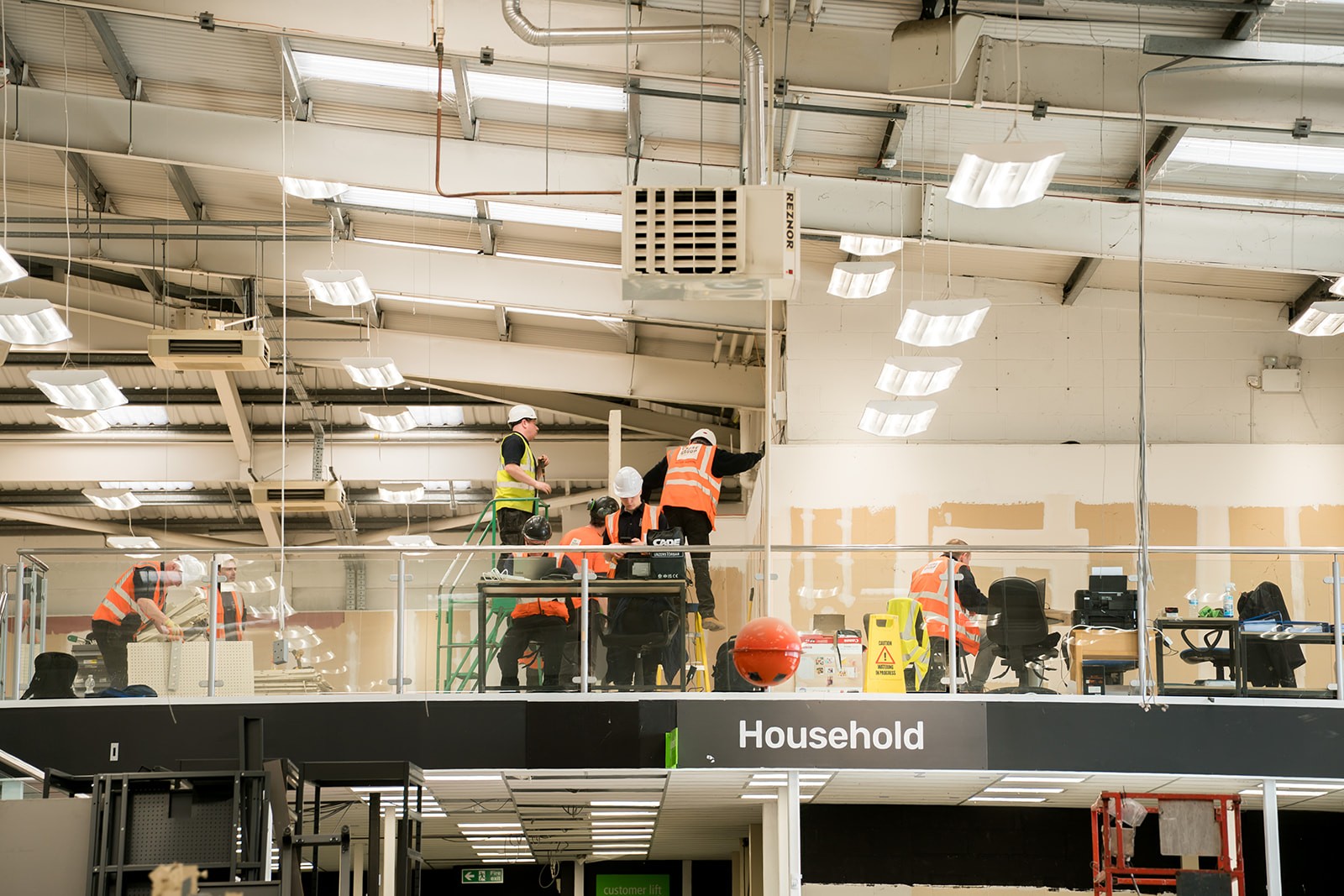 A group of construction workers wearing high-visibility jackets and hard hats celebrate at a construction site with safety signs and equipment visible in the background.
