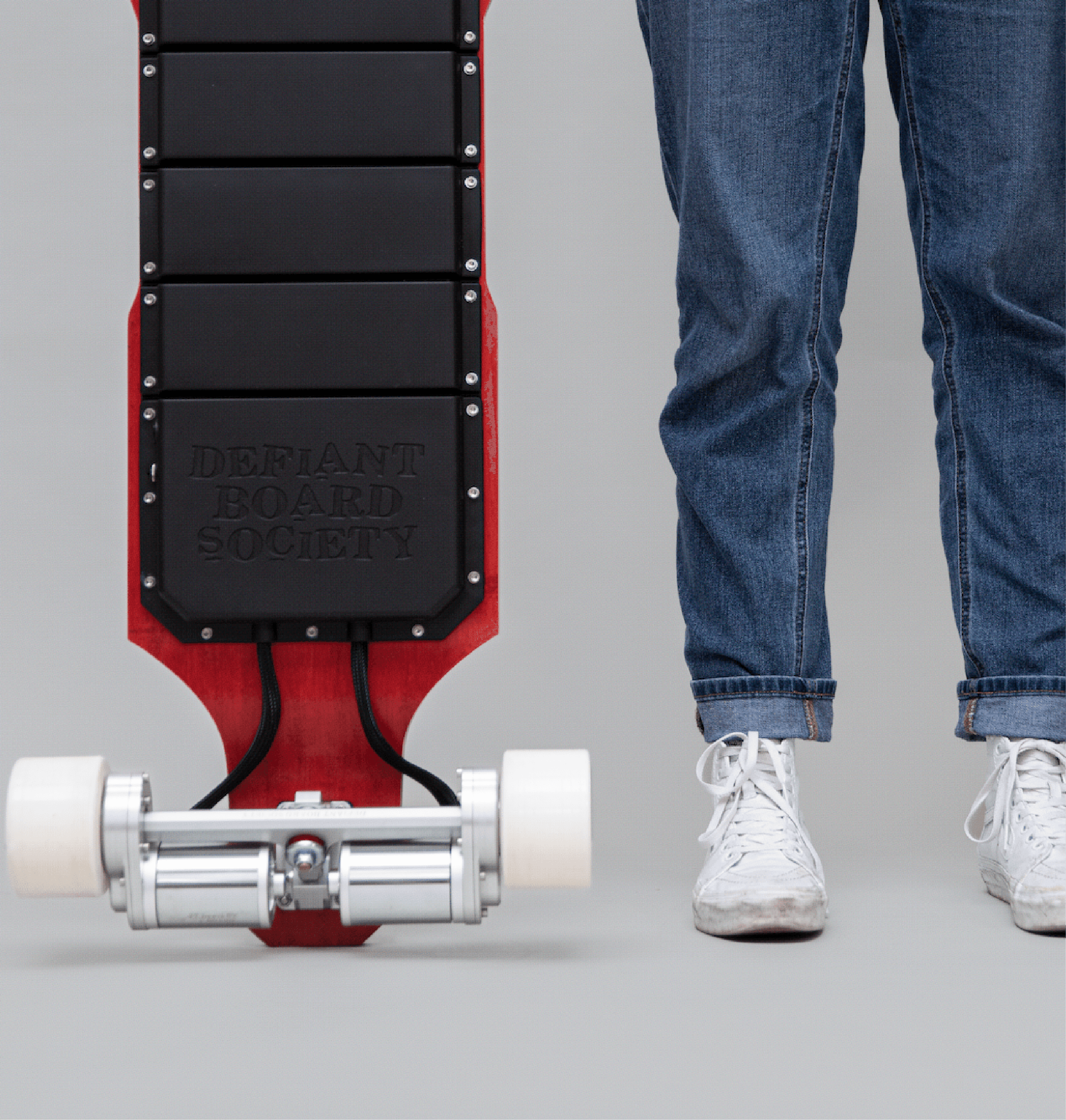 Close-up of electric skateboard wheels and deck next to person wearing jeans and white sneakers