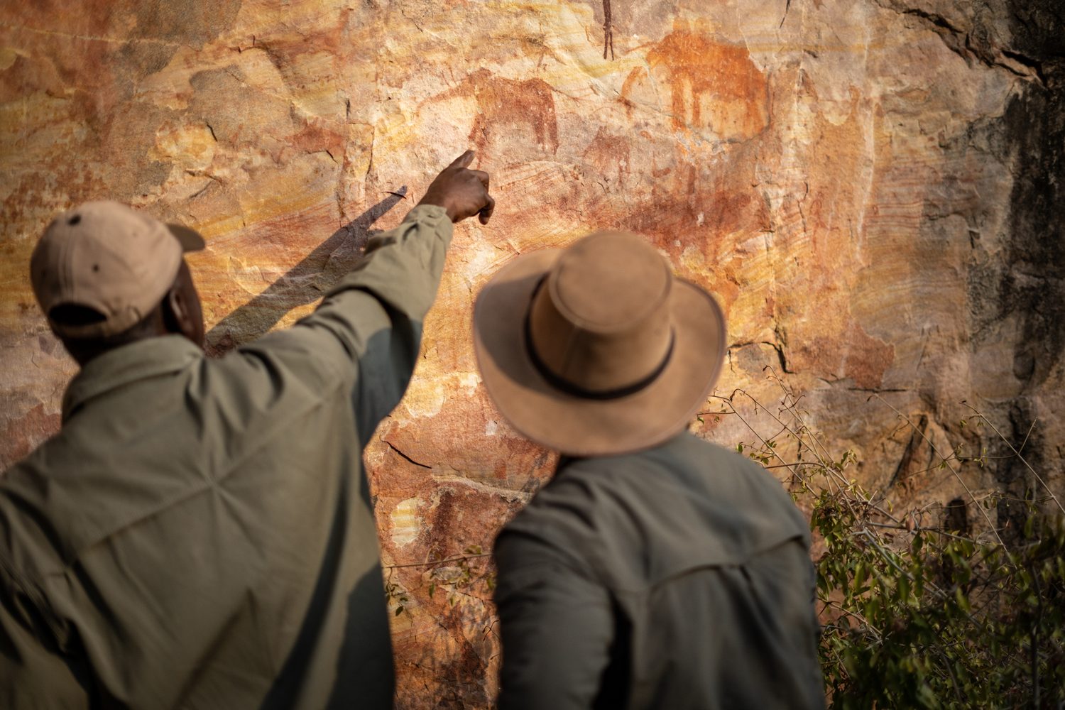 A guide pointing out ancient rock art on a sandstone wall