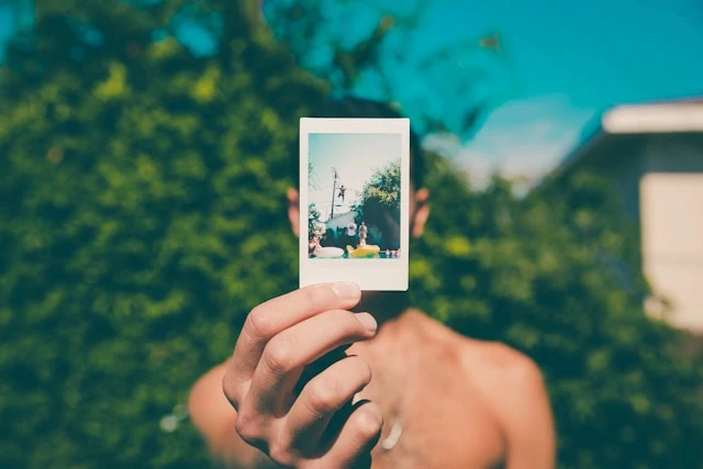 photo of a shirtless man holding an instant photo covering his face