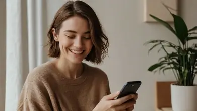 A smiling person using a smartphone in a cozy setting, representing a relaxed and enjoyable online shopping experience with Whisprice.