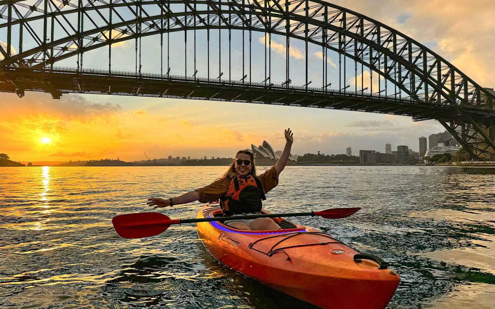 Group of people enjoying a sunrise paddle on Sydney Harbour with a breakfast spread on the kayak, with the iconic Sydney Opera House in the background
