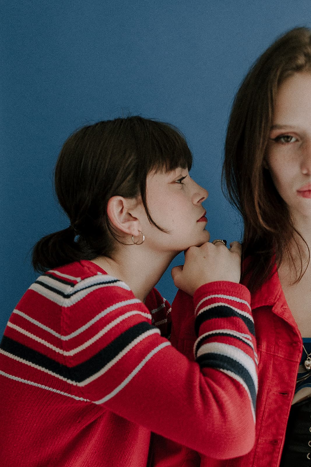 Two models in red outfits pose side by side against a blue background at Revelator Studio in Shreveport, highlighting 90s vintage fashion.