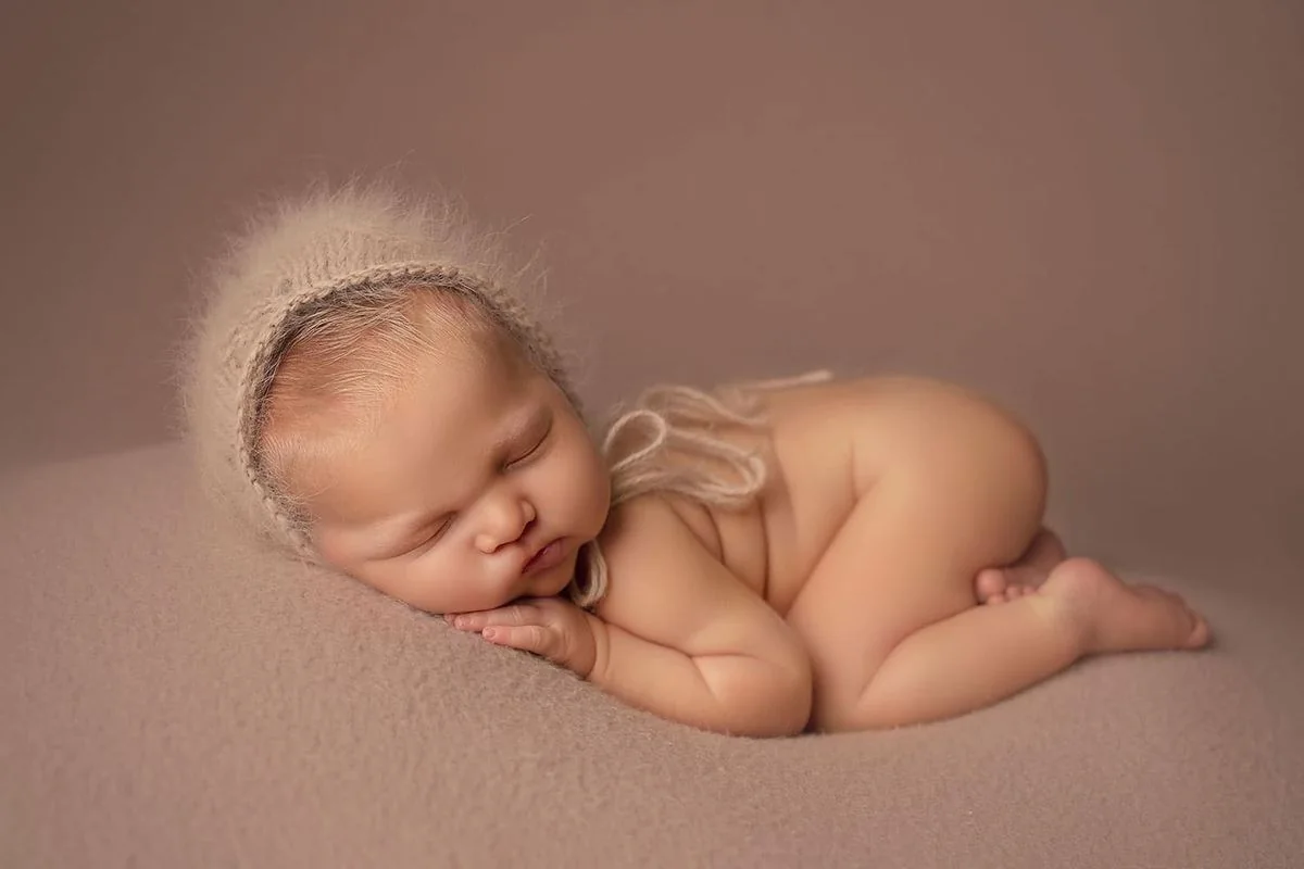 Sleeping newborn with hands under the cheek on a taupe blanket