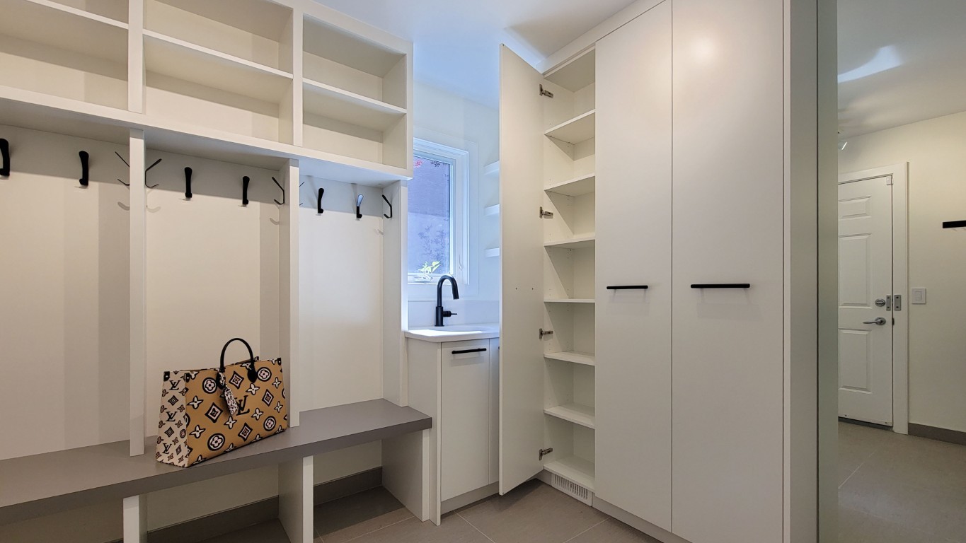 A bright mudroom with built in benches and hooks and enclosed shoe storage. The millwork is white with black hardware.