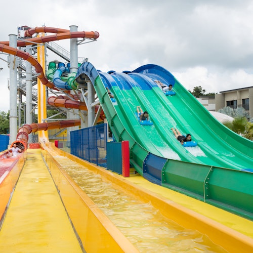People sliding down colorful water slides at a water park on a cloudy day.