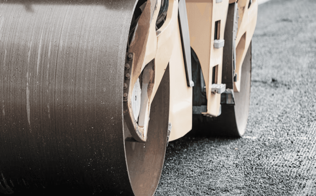 Close-up of a road roller compacting asphalt on a construction site, showcasing its large drum and textured surface.