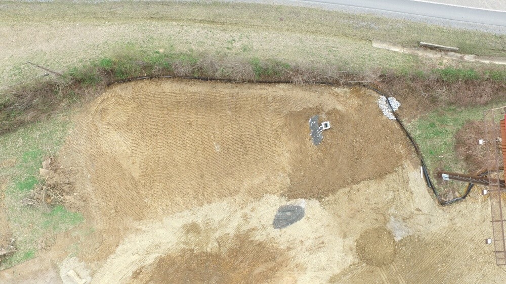 Overhead shot of vacant lot graded to dirt with silt fence around one side.