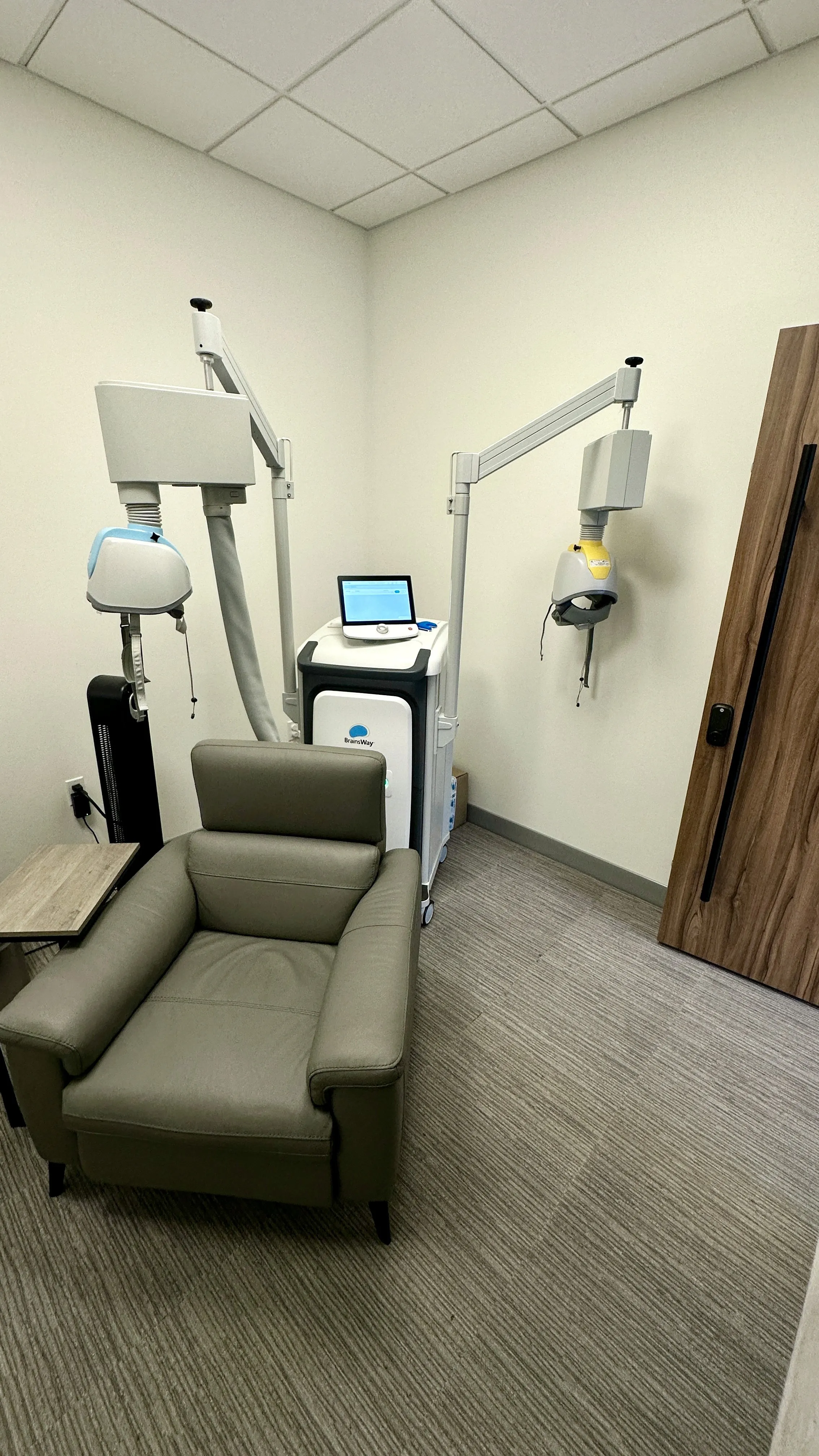 Deep TMS treatment device with coil beside a leather recliner chair next to a wood-paneled door